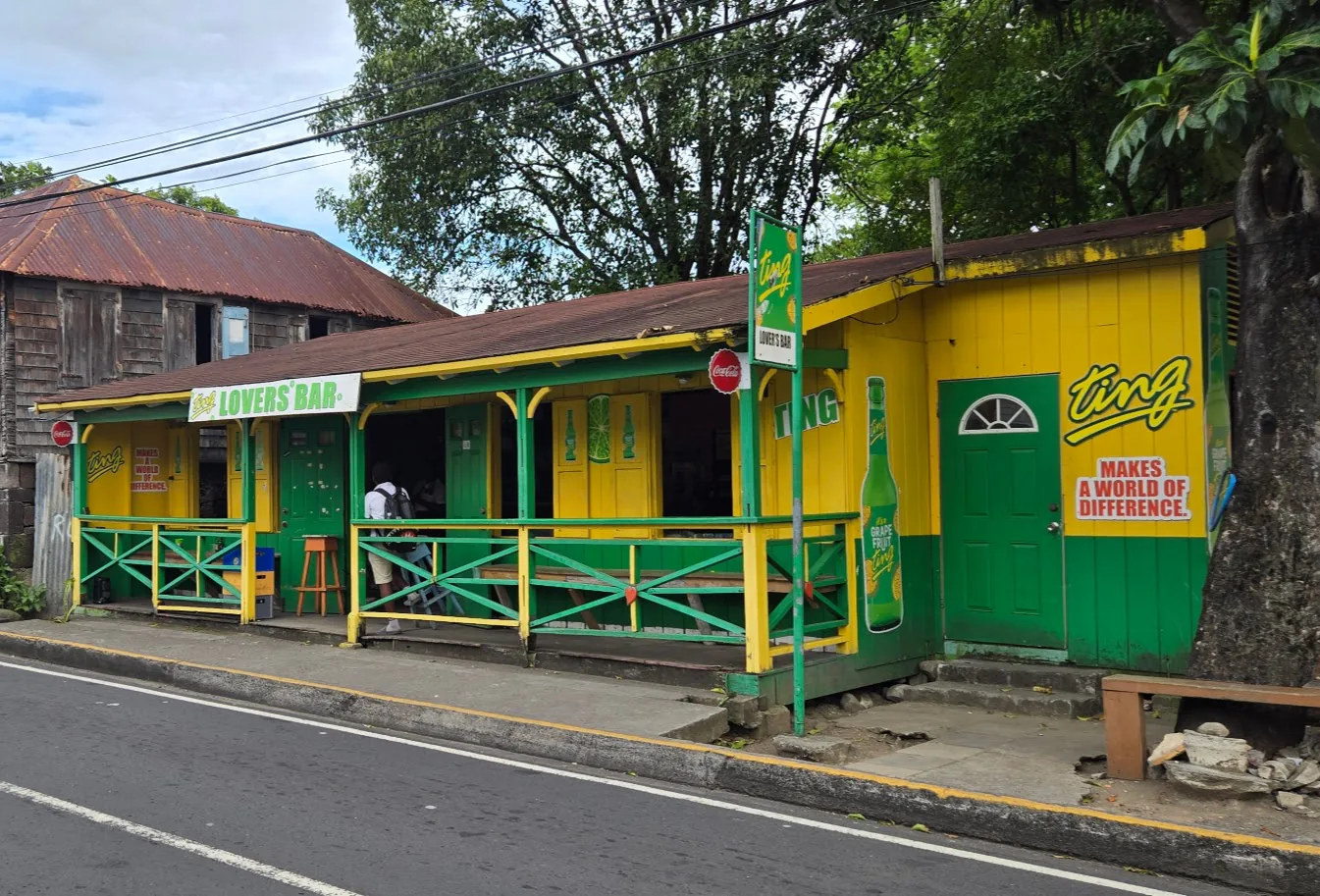 A yellow and green roadside bar with a shaded veranda and wooden railings.