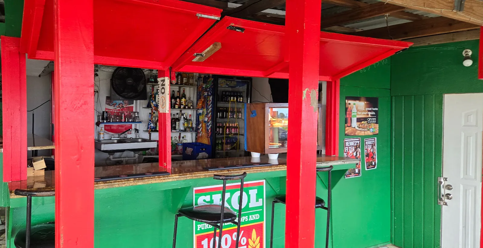 A local bar counter framed by bright red posts, green panels and shelves of drinks.