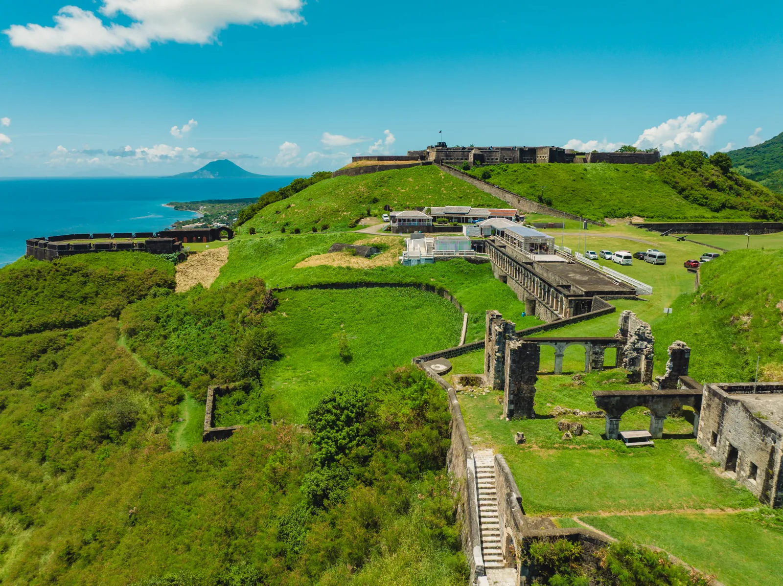 Aerial view of Brimstone Hill’s stone fortress, green slopes and paths overlooking the St. Kitts coastline.
