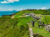 Aerial view of Brimstone Hill’s stone fortress, green slopes and paths overlooking the St. Kitts coastline.