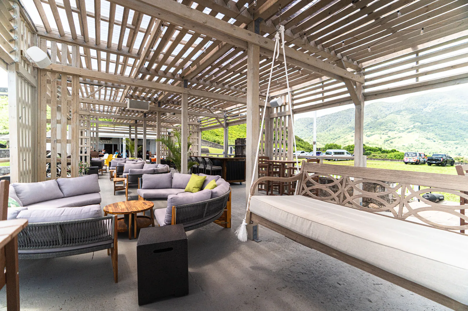 Sofas and a hanging bench beneath the timber canopy at Gibraltar Gastrolounge, with mountain views outside.