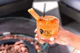An orange drink with a citrus garnish in a Gibraltar Gastrolounge glass, held beside the lounge seating.