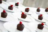 Individual dark cakes topped with red garnishes on white plates at Carambola.