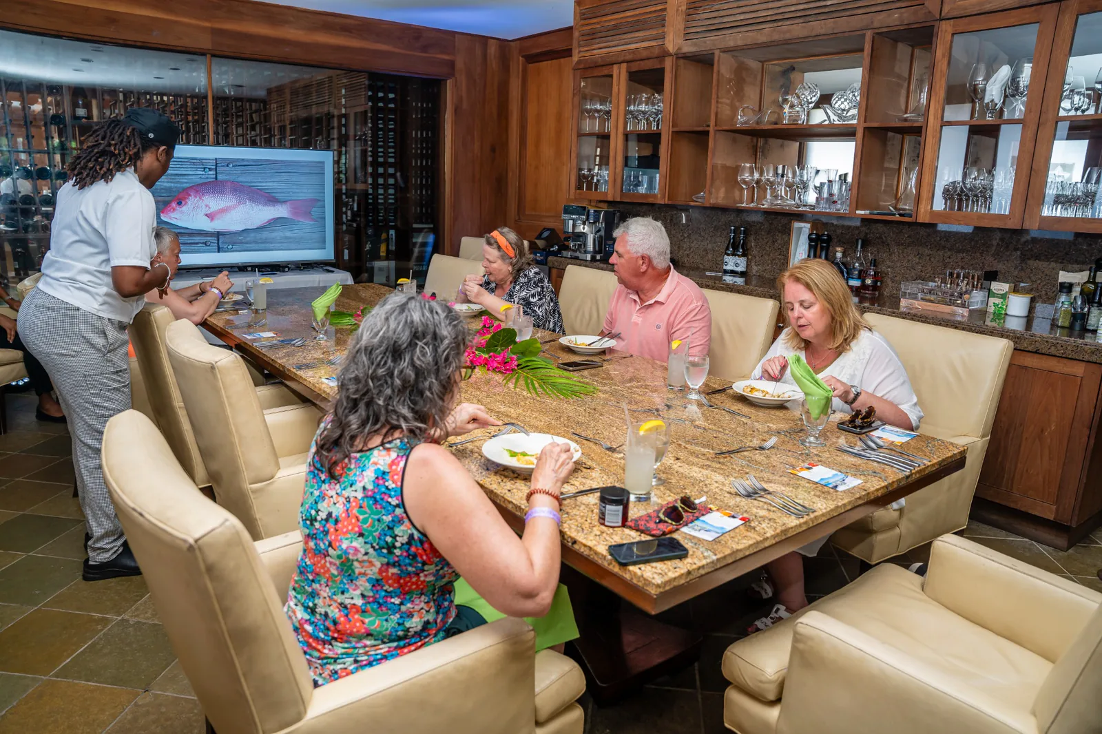 A host talks with foodie tour guests seated around an indoor dining table at Carambola.