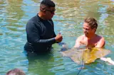 A guide and guest meet a stingray in the shallow lagoon water.