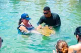 A guide assists a guest with a stingray while other visitors watch.