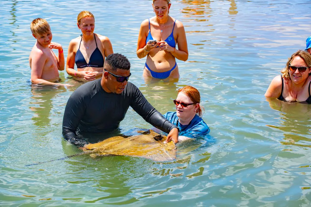 A guide supports a stingray beside a guest as a group watches.